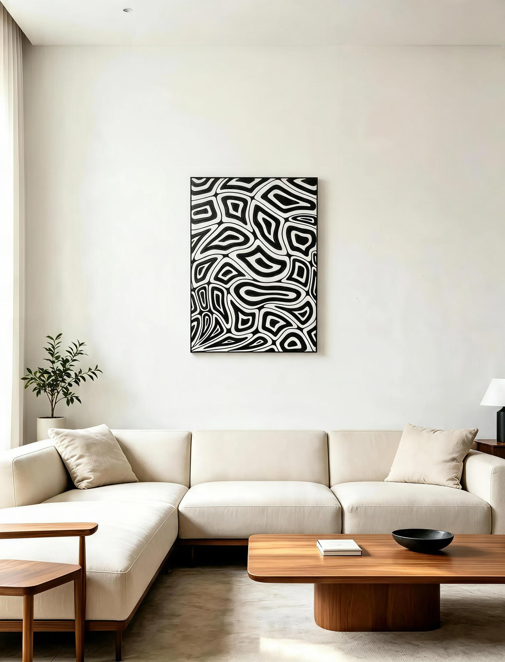 Black and white abstract organic pattern art print in black frame displayed in minimalist white living room above cream sectional sofa